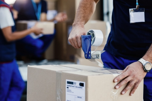 primer plano repartidor cerrando caja carton cinta mientras prepara paquetes su envio